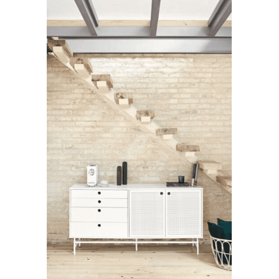 El aparato pequeño en Metal y DM Punto 2P4C, de diseño moderno con cajones y puertas, está colocado contra una pared de ladrillo bajo una escalera de madera. A la derecha, un toque acogedor lo añaden las almohadas estilo industrial en una cesta.