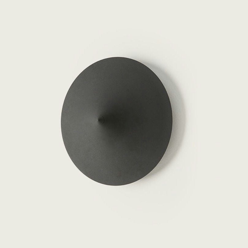 Aplique de pared Hat es una lámpara de pared minimalista, circular, de color gris oscuro, con un centro cónico sobre un fondo claro, que encarna un diseño moderno.