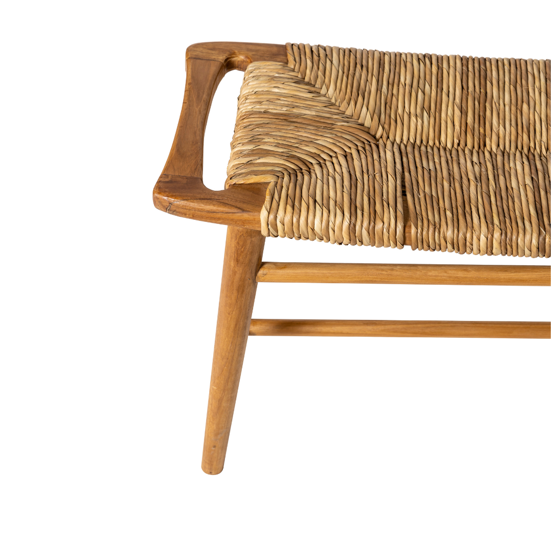 Primer plano de la Banqueta de Madera de Teca y Ratán Anyam (120 cm), que muestra su asiento de ratán, sus robustas patas de madera de teca y su diseño de esquina en ángulo sobre un fondo blanco.