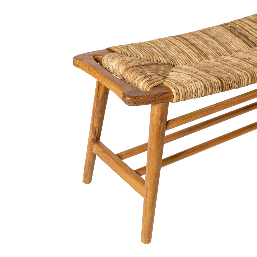 La Banqueta de Madera de Teca y Ratán Anyam (120 cm) aparece en vista lateral angular, mostrando su asiento de ratán tejido, sobre un fondo blanco.