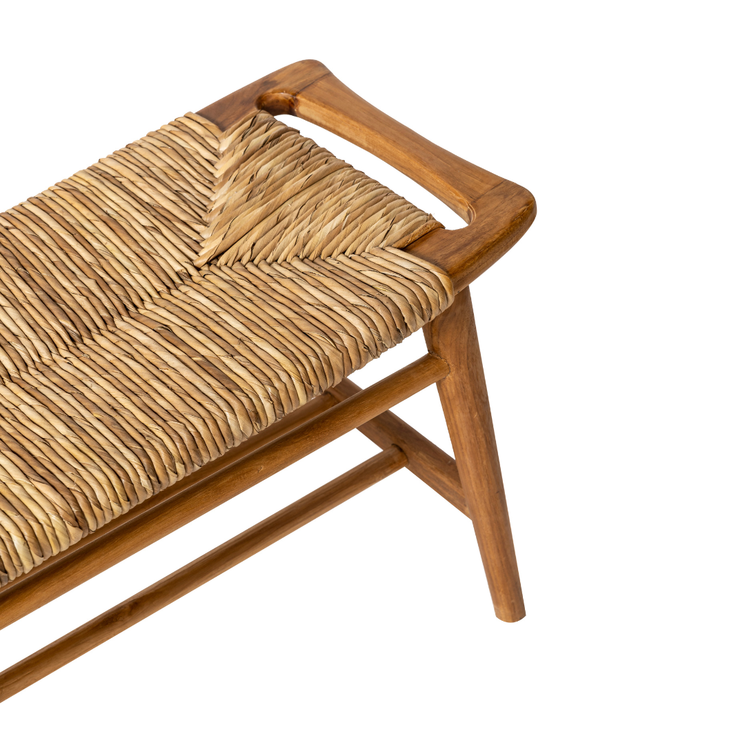 Un primer plano de la Banqueta de Madera de Teca y Ratán Anyam (120 cm) muestra su estructura de teca y asiento de ratán, resaltando parte del respaldo y las patas sobre un fondo blanco.