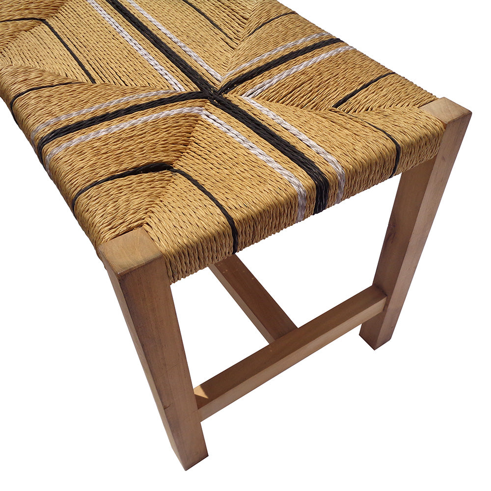 La Banqueta en Madera de Teca y Ratán Korea cuenta con un asiento de fibra natural tejida con rayas geométricas en blanco y negro, que combina un diseño moderno rústico con una artesanía duradera y elegante en madera de teca.