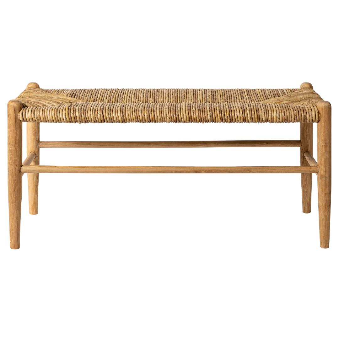 La Banqueta en Madera de Teca y Ratán Manado es un banco rectangular con un asiento de ratán natural tejido y cuatro patas rectas de madera de teca, que se muestra sobre un fondo blanco liso.