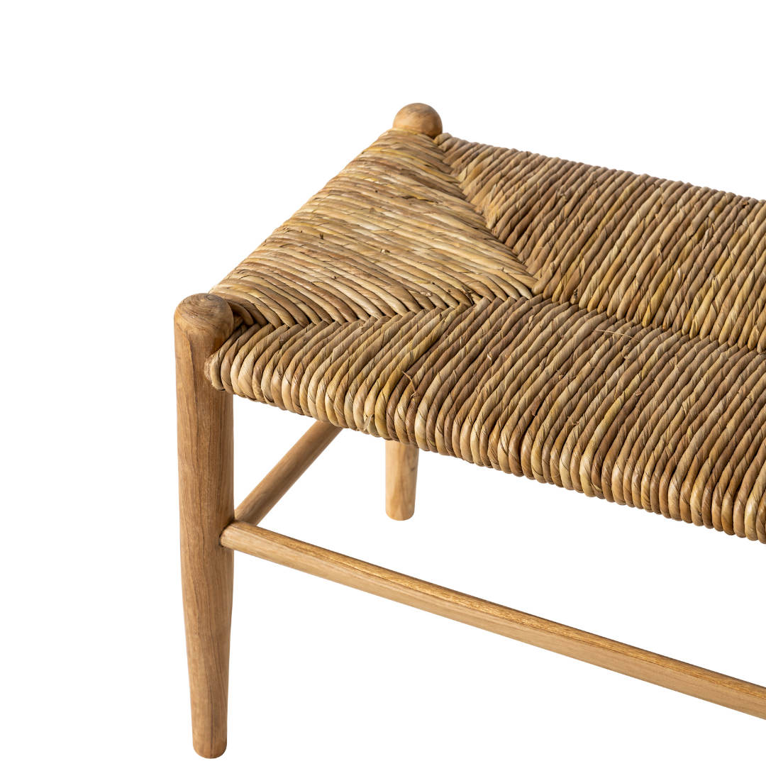 Primer plano de la Banqueta en Madera de Teca y Ratán Manado, que muestra la construcción en madera de teca y un asiento de ratán natural tejido con esquinas y patas detalladas sobre un fondo blanco.