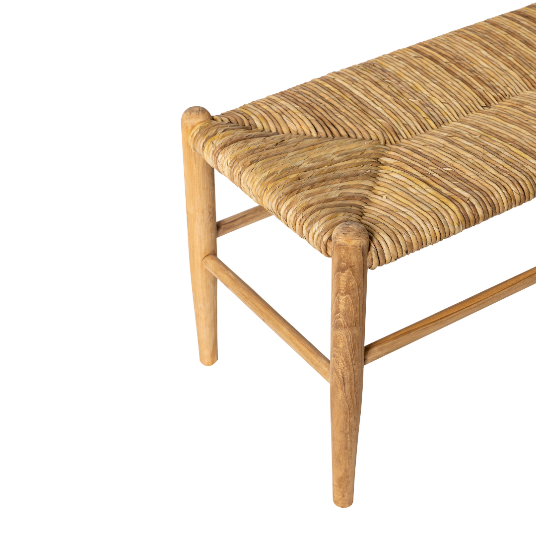 Un primer plano de la Banqueta en Madera de Teca y Ratán Manado, destacando su estructura de madera de teca, su asiento de ratán natural tejido y sus patas en ángulo sobre un fondo blanco.