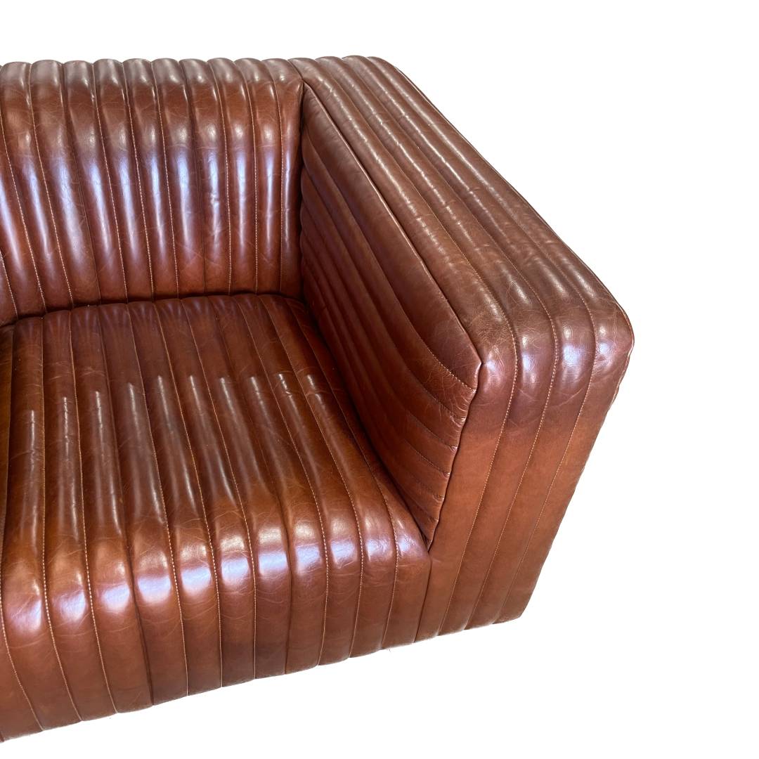 Detalle del Sillón en Cuero y Madera Bristol, con tapicería de piel acanalada vertical y un moderno diseño cuadrado, sobre fondo blanco.