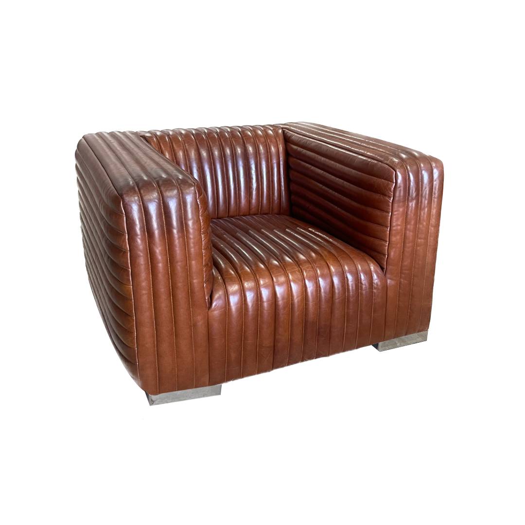 El Sillón en Cuero y Madera Bristol presenta tapizado acanalado vertical, diseño industrial moderno, patas metálicas y silueta cuadrada. Fotografiado sobre fondo blanco.