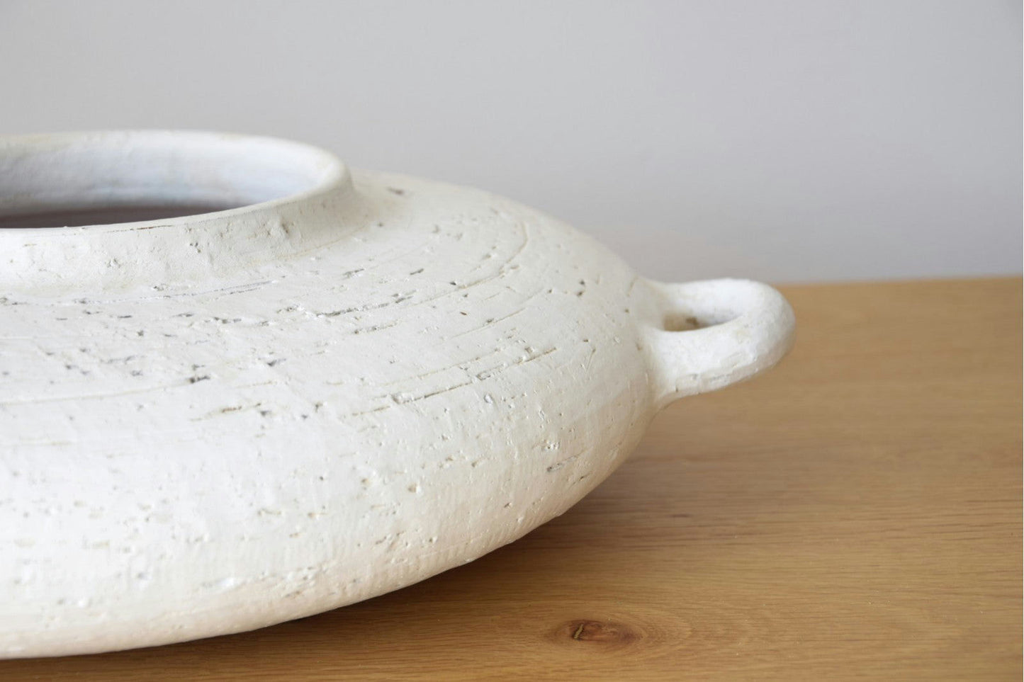 Un primer plano del Centro de Mesa Cerámica Ilda en Blanco Pátina, con acabado texturizado y tirador, apoyado sobre una superficie de madera.