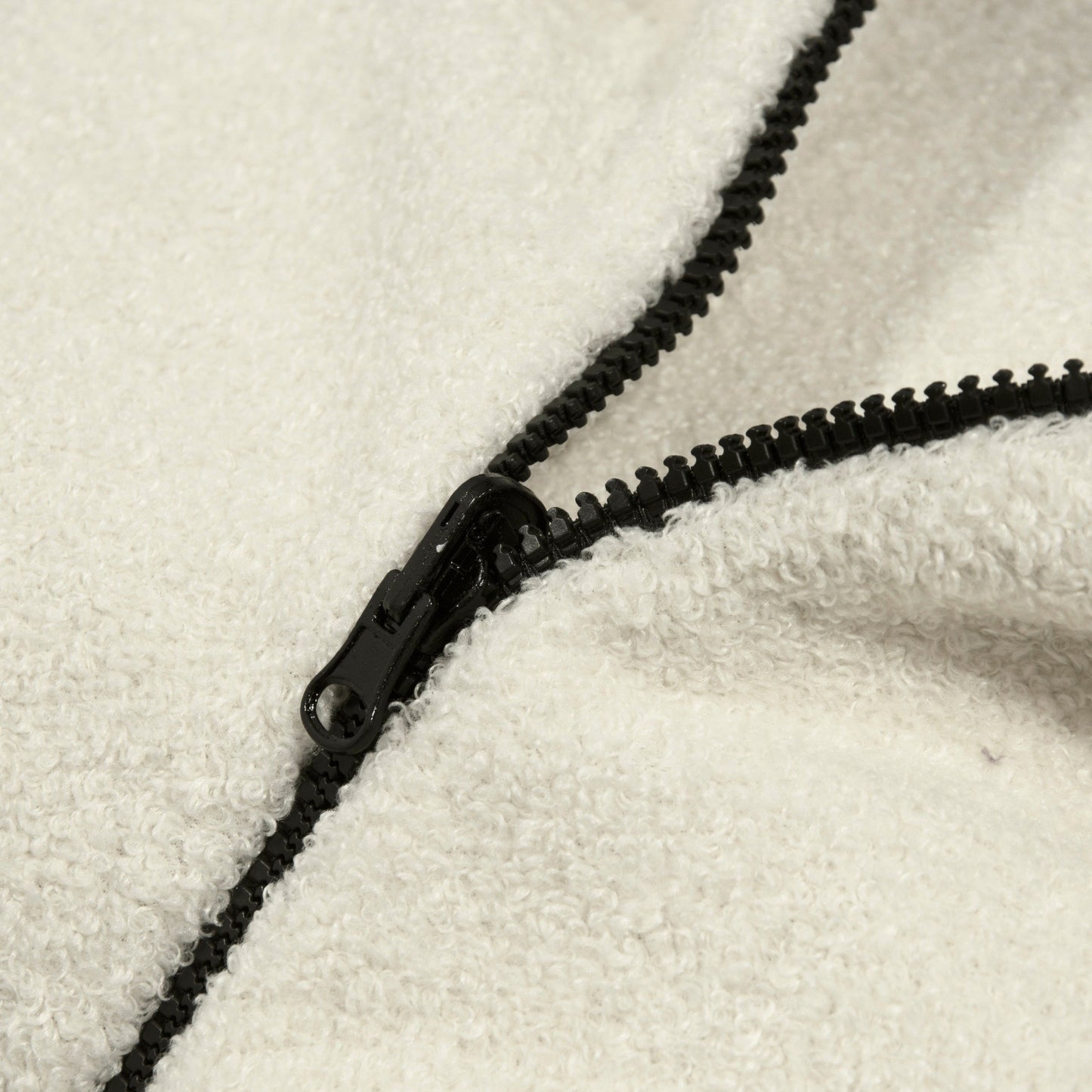 Detalle de una cremallera negra parcialmente abierta sobre el tejido blanco texturizado del Bean bag puff de tela borreguito COCOON 100 TEDDY (100×55×60 cm), destacando su comodidad ergonómica para salón, dormitorio o sala de juegos.