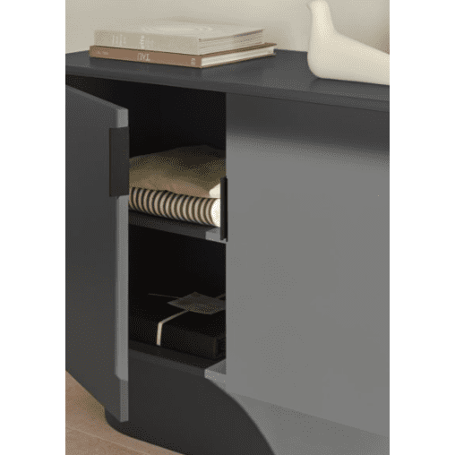 El mueble abierto con dos estantes muestra el almacenamiento ordenado con telas a rayas apiladas y una pequeña caja negra. En la parte superior se encuentran libros y un objeto decorativo, que complementan el diseño moderno de la Cómoda en MDF con 2 Puertas Totem 2P.