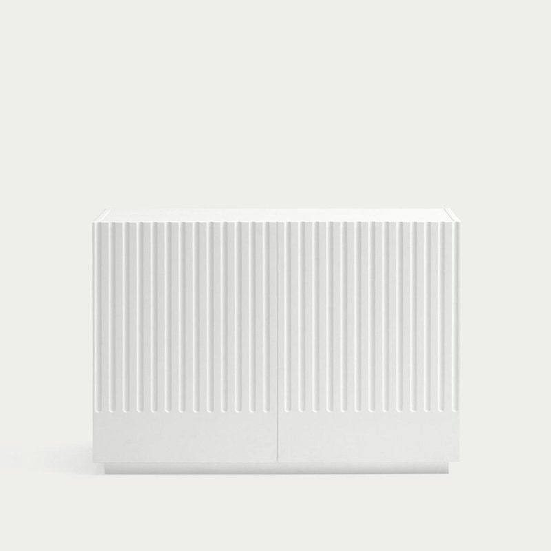 La Cómoda en MDF con 2 Puertas y 2 Cajones Doric 2P2C es un mueble de almacenaje minimalista de color blanco con un frente ranurado verticalmente sobre un fondo gris claro, ideal para un almacenamiento inteligente.