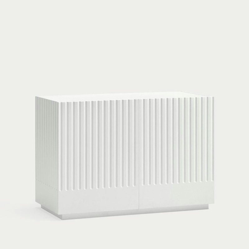 La Cómoda en MDF Doric 2P2C presenta un diseño rectangular blanco con ranuras verticales en el frente, incorporando un diseño minimalista, ofreciendo almacenamiento con sus 2 puertas y 2 cajones.