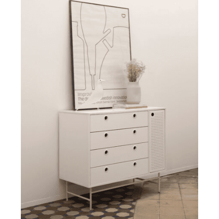 Una elegante Cómoda en MDF con 4 Cajones y Puerta en Metal Punto 1P4C se encuentra contra la pared, rematada con una lámina enmarcada y un jarrón con flores secas. Los hermosos azulejos estampados del piso realzan el atractivo estético de la habitación.