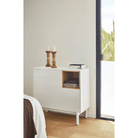 La cómoda de MDF y roble con 4 cajones Corvo 4C ofrece un almacenamiento eficiente con un pequeño estante abierto para ropa doblada, cubierto con velas y libros. Su diseño moderno complementa la gran ventana cercana, que ofrece una vista serena de los árboles del exterior.
