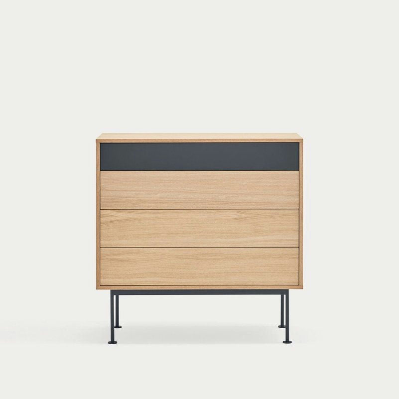 La Cómoda en MDF y Roble con 4 Cajones Yoko 4C, con sus delgadas patas de metal negro y cuatro cajones, personifica el diseño minimalista sobre un fondo sencillo, proporcionando soluciones de almacenamiento contemporáneas.