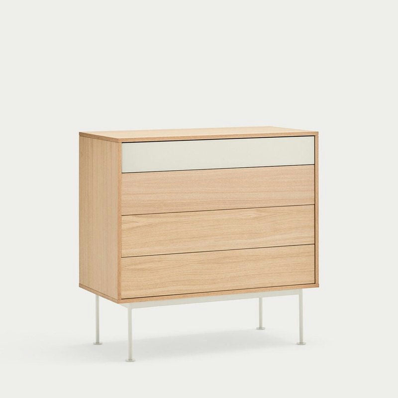 La Cómoda en MDF y Roble con 4 Cajones Yoko 4C es una pieza de almacenamiento minimalista con tres cajones de roble, un cajón de MDF con cubierta blanca y elegantes patas de metal blanco, capturando un diseño minimalista contemporáneo sobre un fondo sencillo.