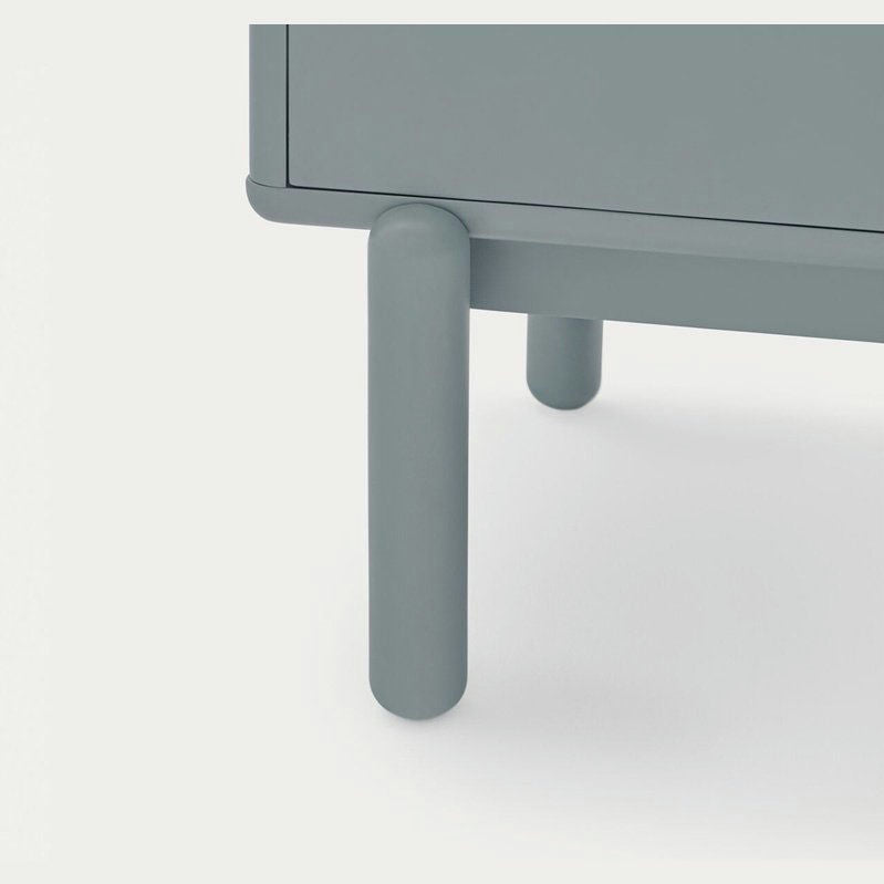 Primer plano de la Cómoda en MDF y Roble con 7 Cajones Corvo 7C, un mueble verde con patas lisas y cilíndricas sobre un fondo liso.