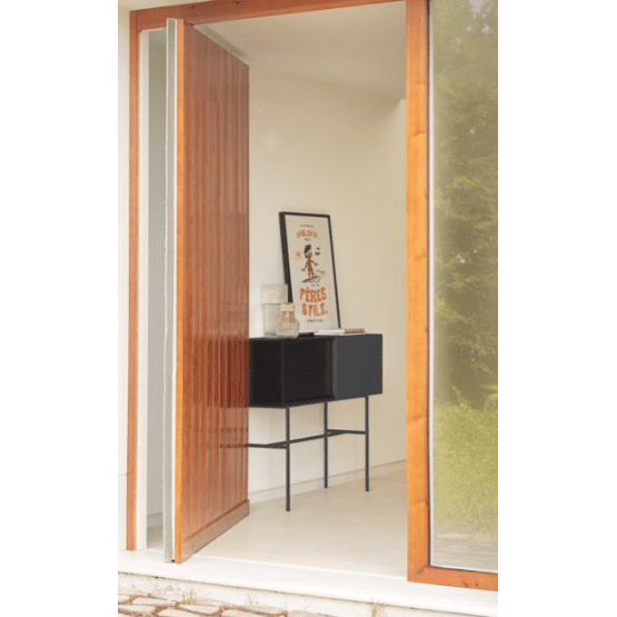 Una puerta de madera se abre a una habitación luminosa, que muestra el elegante diseño contemporáneo de la Consola Nube 1P2C en su acabado negro, rematado con un póster enmarcado.