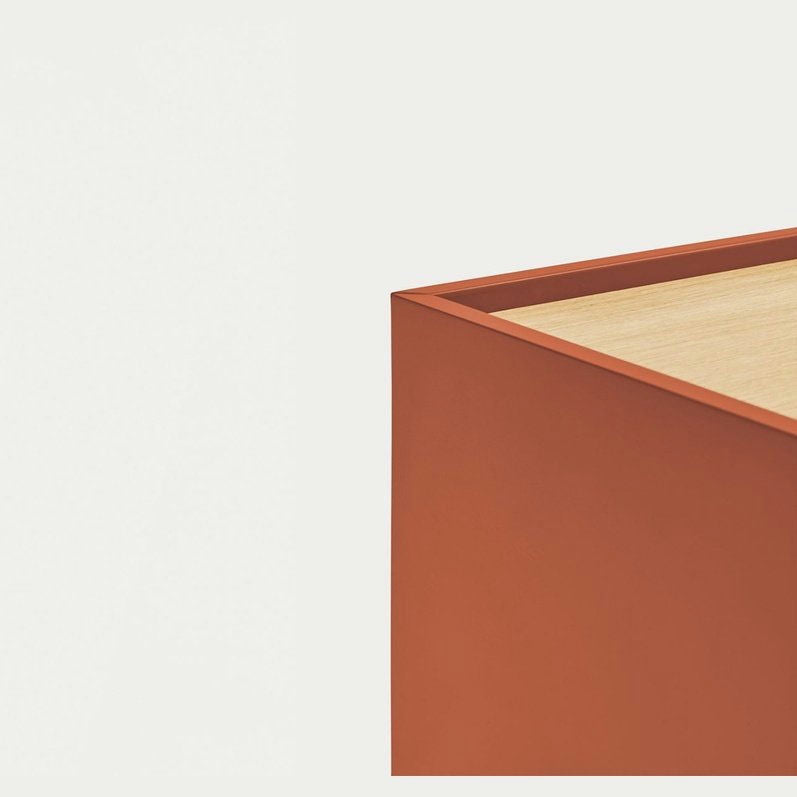 La esquina de una caja rectangular de color naranja con tapa de madera resalta la modernidad y funcionalidad de la Consola Otto 2P2C (Suspendida) sobre un fondo liso y claro.