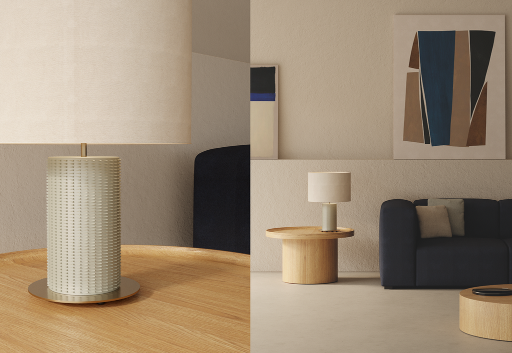 Un salón moderno con una mesa auxiliar redonda de madera que sostiene la Lámpara de mesa en Cerámica y Metal Dab, colocada junto a un sofá oscuro y arte abstracto en una pared beige.