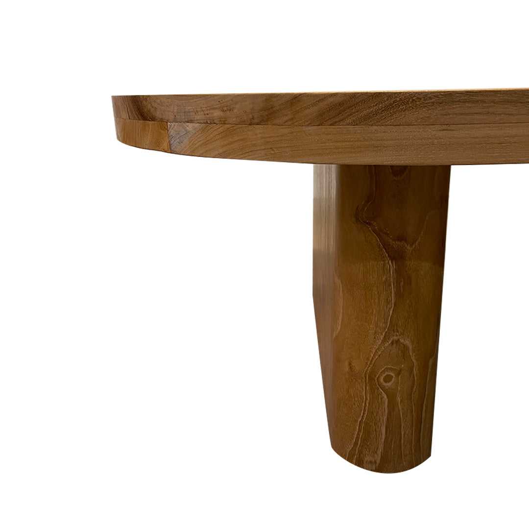 Primer plano de una mesa de madera que muestra la Mesa de centro en madera de teca (140x90 cm) María, que cuenta con una superficie redonda y una pata cilíndrica. Elaborada a partir de teca fina, muestra con elegancia su acabado natural y las intrincadas vetas de la madera, lo que encarna un diseño sofisticado.