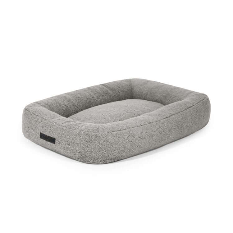 Se muestra una Cama para perro de tela borreguito 75×60×18 cm - DOG BED 75 TEDDY rectangular de color gris claro con bordes elevados y tejido suave y texturizado sobre un fondo blanco liso.