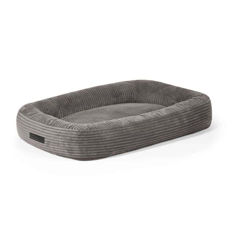 La Cama para perro de terciopelo acanalado 75×60×18 cm - DOG BED 75 WAVES cuenta con laterales elevados y una base plana acolchada para mayor comodidad y estilo, mostrada aquí en gris sobre fondo blanco. Esta cama también es hipoalergénica.