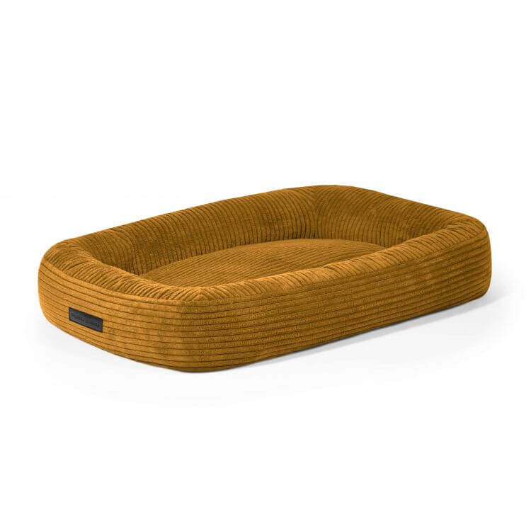 La Cama para perro de terciopelo acanalado 75×60×18 cm - DOG BED 75 WAVES es una cama rectangular para perros de color amarillo mostaza con bordes elevados y base acolchada, que ofrece estilo y comodidad hipoalergénica sobre un fondo blanco.