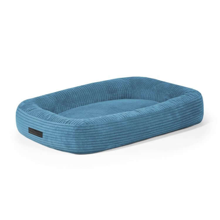 Una Cama para perro de terciopelo acanalado 75×60×18 cm - DOG BED 75 WAVES azul rectangular con bordes en relieve y centro acolchado, mostrada sobre fondo blanco.
