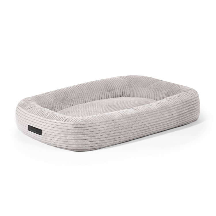 Cama para perro de terciopelo acanalado 75×60×18 cm DOG BED 75 WAVES en tono gris claro, diseño rectangular con bordes elevados y acceso bajo al frente, sobre fondo blanco.