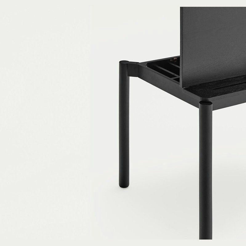 Primer plano del Escritorio de Madera Atlas, una silla minimalista negra con asiento rectangular y delgadas patas cilíndricas, que representa el Diseño Moderno sobre un fondo liso.