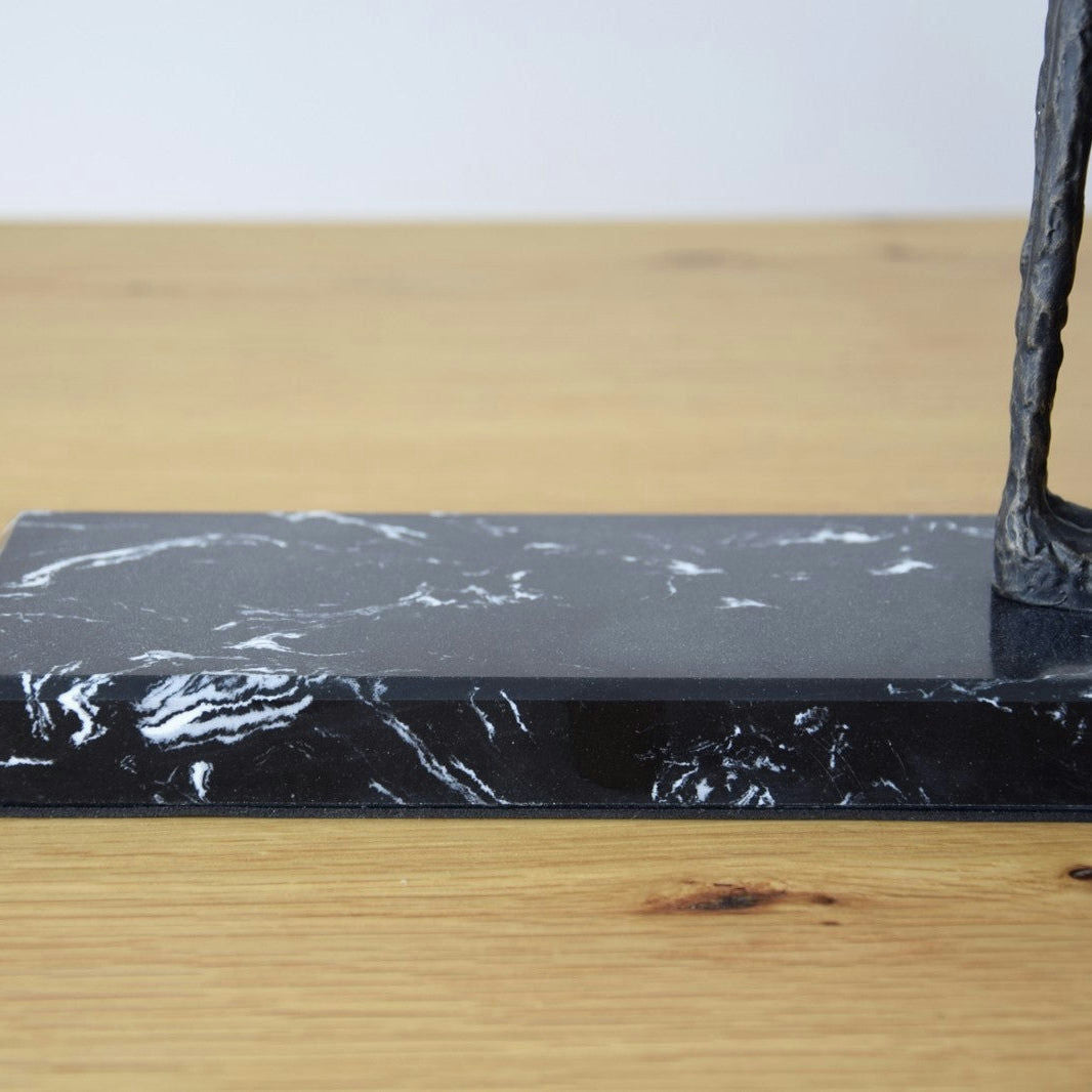 La Escultura Buscando en Metal y Mármol presenta una superficie de madera clara con una base de mármol y un detalle escultórico de bronce, que encarna la elegancia atemporal en el diseño de interiores.