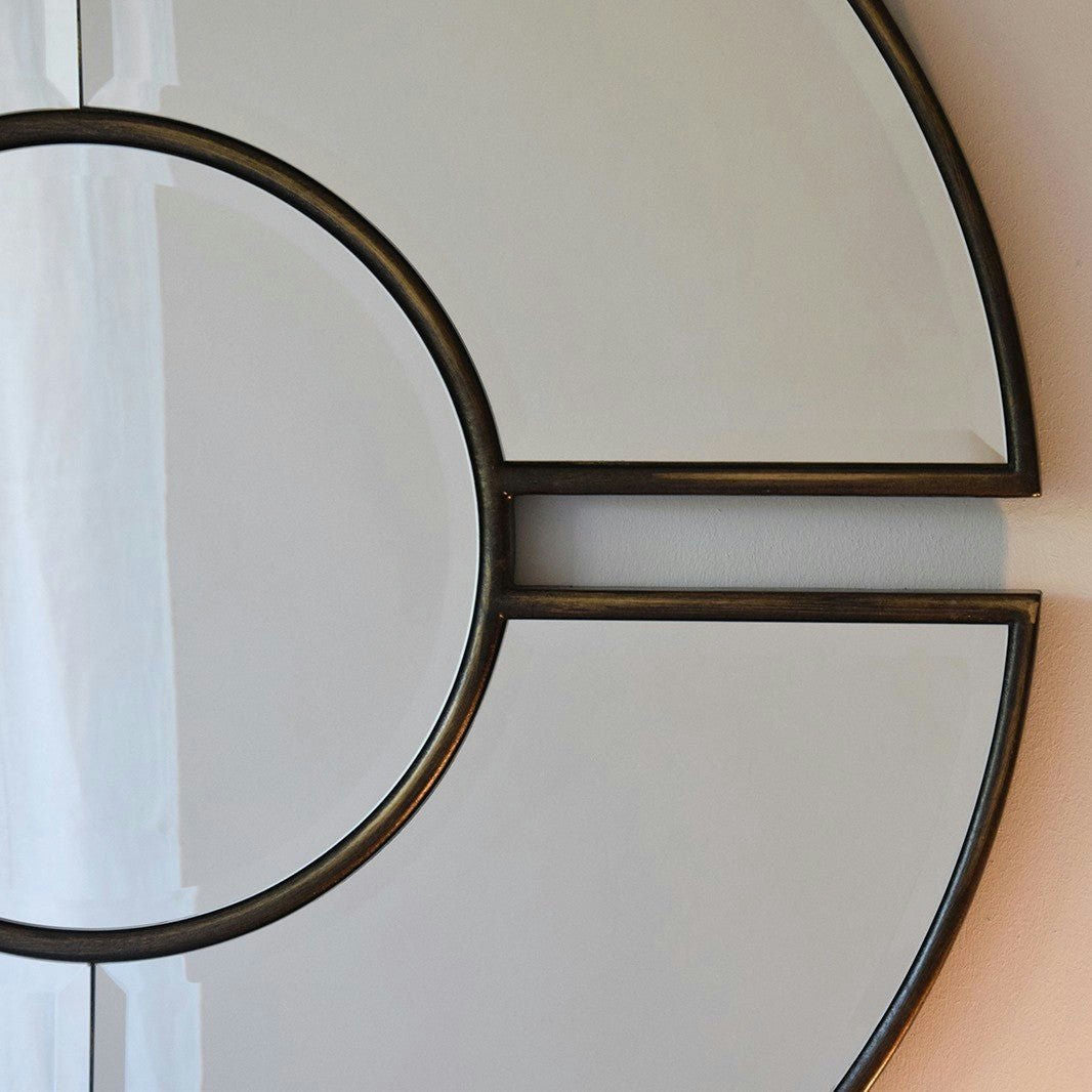 Primer plano del Espejo Redondo Reflejo Doré, que presenta un diseño de panel circular y semicircular, que irradia elegancia y sofisticación mientras está perfectamente montado en una pared.