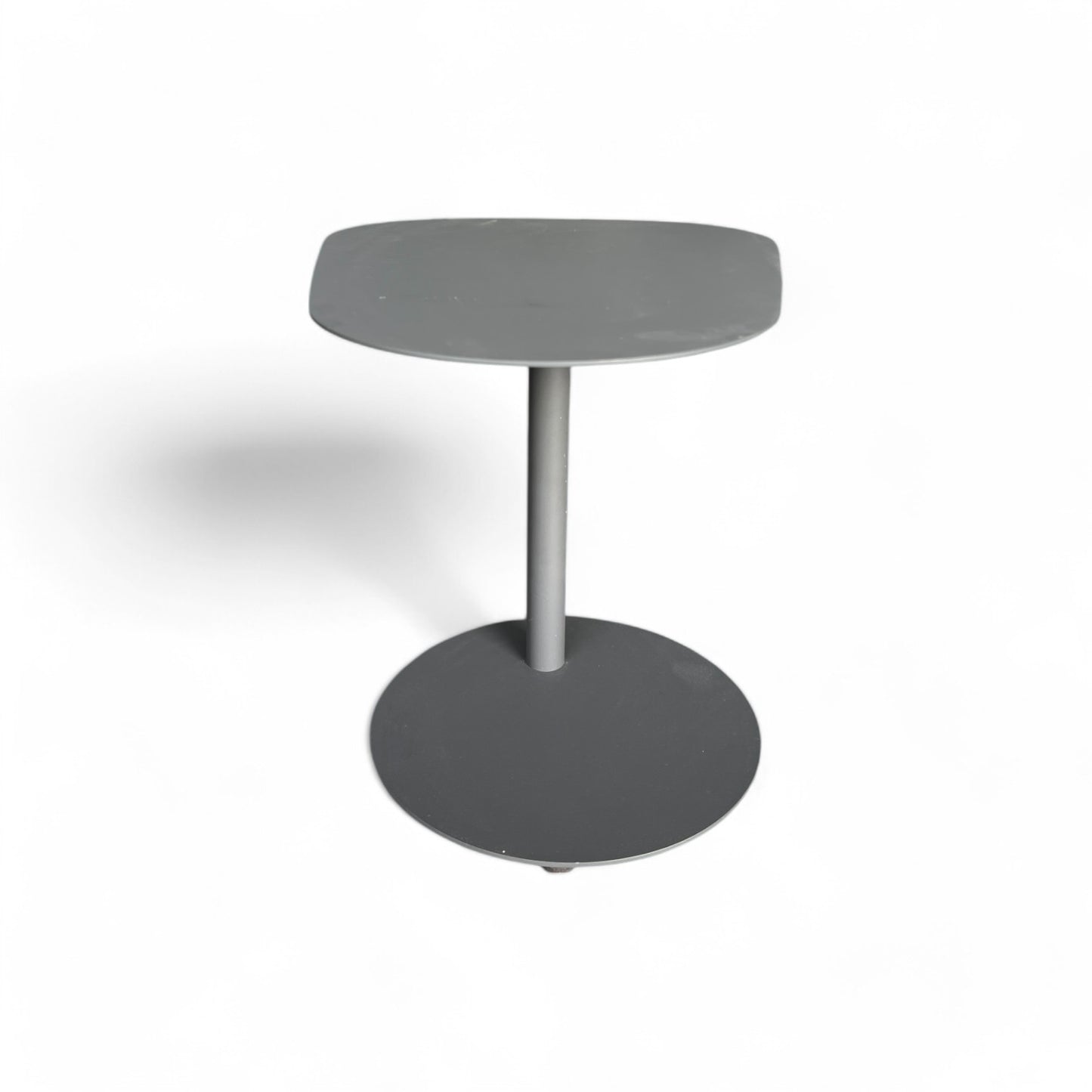 La Mesa auxiliar de exterior aluminio antracita 53 × 38 × 50 cm INDIGO, de estilo moderno, tiene base redonda, soporte central y tapa rectangular en gris, ideal para jardín o patio, sobre fondo blanco.