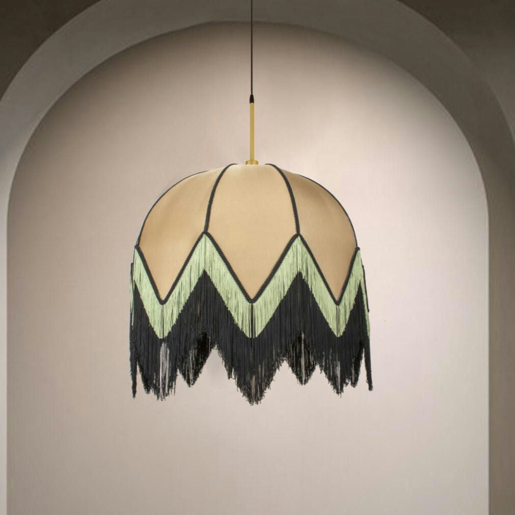 La Lámpara de Techo Colgante Vintage de Flecos CafeLatte 30159, con una pantalla beige en forma de cúpula y un diseño de flecos en zigzag negros y verdes, irradia un encanto de estilo retro mientras cuelga elegantemente contra una pared arqueada.