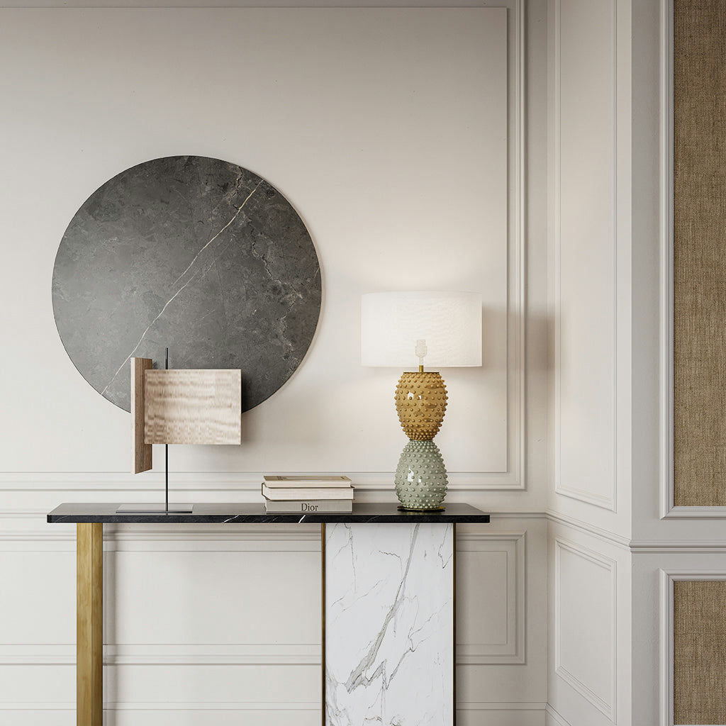 Un interior moderno que presenta la lámpara de mesa Cactus NAC135/2 con una base texturizada, una pieza decorativa de mármol redondeada y libros apilados sobre una mesa consola contra una pared con paneles. El diseño moderno se realza al agregar un pequeño cactus para lograr una elegancia natural.