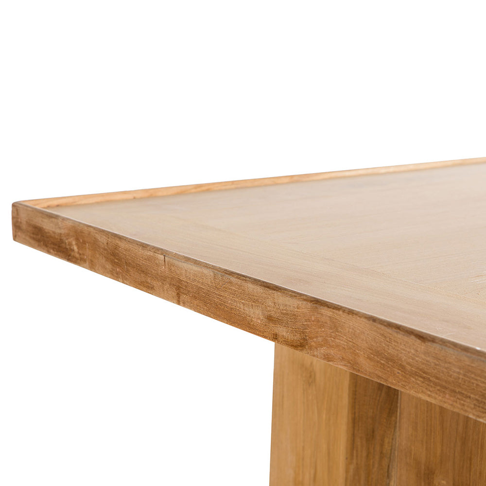 Primer plano de una mesa de madera rectangular en esquina con vetas y textura visibles, que muestra líneas limpias y un acabado natural. Esta mesa de centro en madera de teca y caucho Cote ejemplifica la elegancia moderna, elaborada con madera de teca de primera calidad para mayor durabilidad y atractivo.