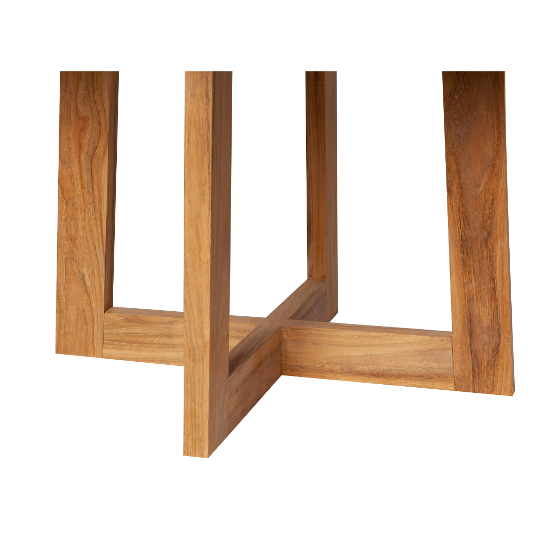 Vista de cerca de las elegantes patas entrecruzadas de la base redonda de madera de Ø120 cm de la mesa Begur, elaborada con un acabado de teca natural.