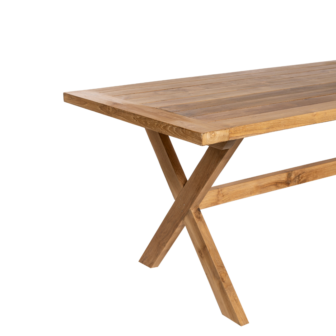 La mesa de comedor en madera de teca para exterior Begur tiene una superficie rectangular y patas en forma de X, elaboradas con madera de teca duradera. Presentada en ángulo sobre un fondo blanco, esta pieza de mobiliario de exterior añade elegancia a cualquier espacio.