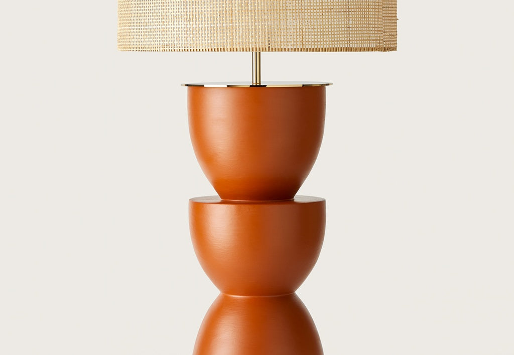 La Lámpara de mesa en Cerámica y Metal Metric cuenta con una base escultural color terracota y pantalla cilíndrica tejida, ideal para decoración moderna sobre fondos lisos.