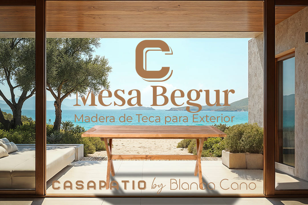 La mesa de comedor en madera de teca para exterior Begur resalta en el mobiliario del jardín, situada en el patio con vistas a la playa y su nombre junto al branding en la puerta de cristal.