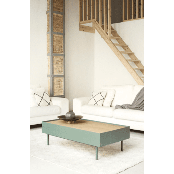 Una sala de estar moderna muestra la Mesa de Centro Arista 2C verde claro, sofás blancos y una alfombra beige, debajo de una escalera de madera que conduce al loft. Este espacio combina diseño inteligente y almacenamiento elegante para lograr estilo y funcionalidad.