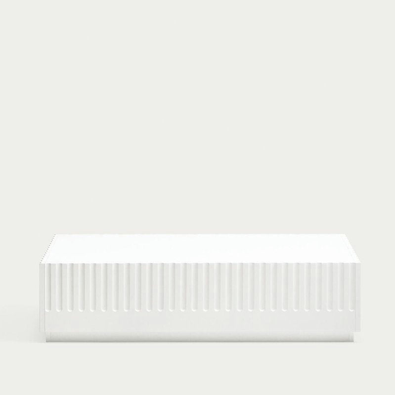 Una caja rectangular blanca, que recuerda el estilo dórico de la Mesa de Centro con sus lados acanalados, reposa sobre un fondo gris claro liso.