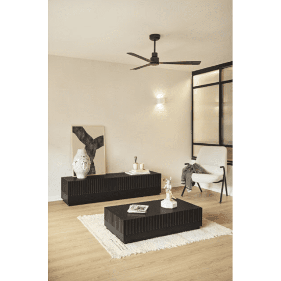 Una sala de estar minimalista con una elegante mesa de centro Doric negra con espacio de almacenamiento oculto. El espacio incluye una consola, un sillón blanco y una decoración moderna. Un ventilador de techo y una lámpara de pared añaden funcionalidad. Los pisos de madera complementan la alfombra blanca, mientras que el arte de la pared se apoya elegantemente sobre la consola.