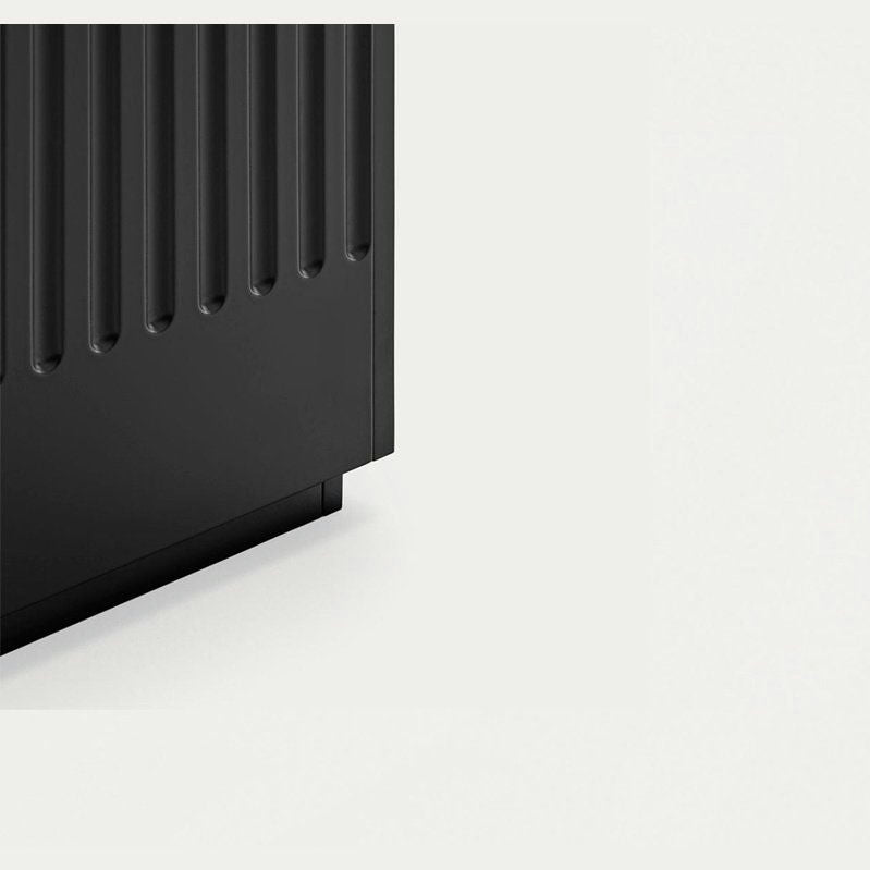 Primer plano de la Mesita de Noche Doric 1C, un electrodoméstico rectangular negro que presenta ranuras verticales que se asemejan a columnas dóricas en un lado, sobre un fondo claro y liso.