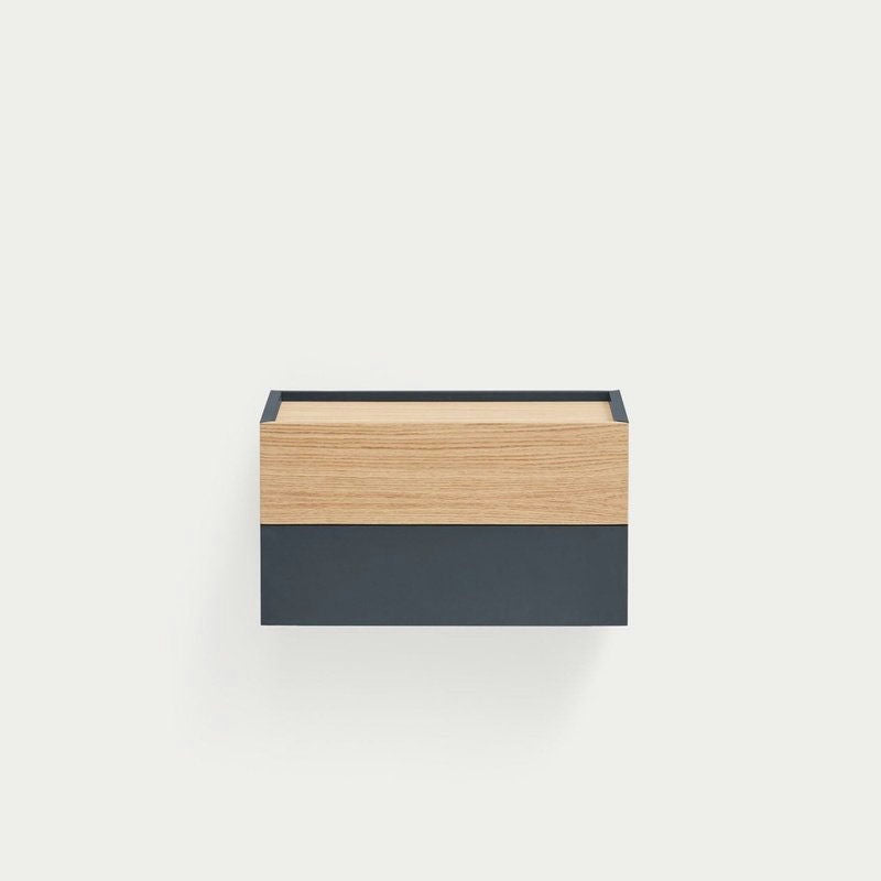 La mesita de noche Otto 2C (Suspendida) es una cajonera minimalista de dos tonos montada en la pared con una parte superior de madera clara y una base gris oscuro. Su diseño flotante ofrece un almacenamiento inteligente, optimizando elegantemente el espacio sobre un fondo liso.