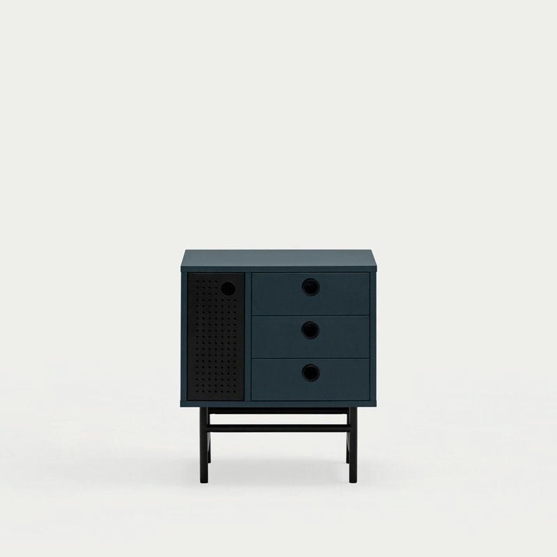 La Mesita de noche Punto 1P3C es un gabinete moderno verde oscuro con tres cajones y una puerta perforada, que brinda diseño contemporáneo y amplio almacenamiento interno, todo sostenido por patas negras cortas sobre un fondo claro liso.