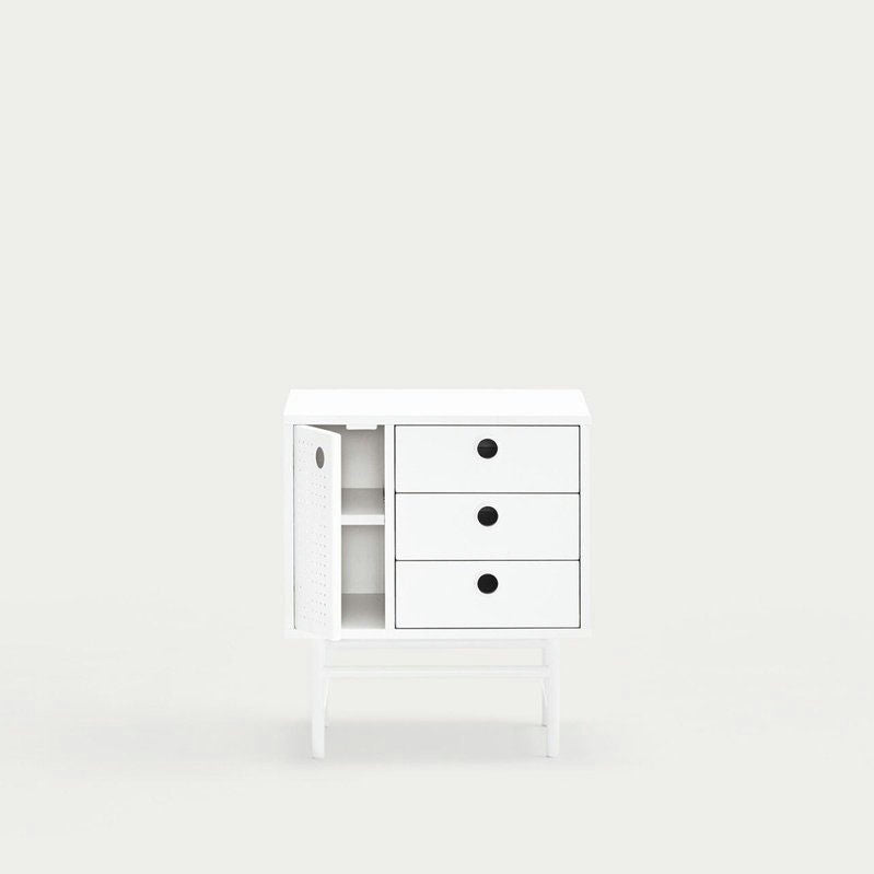 La Mesita de noche Punto 1P3C es un mueble minimalista blanco ideal para usar junto a la cama, que cuenta con tres cajones y una puerta lateral abierta con dos estantes, que se destaca elegantemente sobre un fondo gris claro liso.