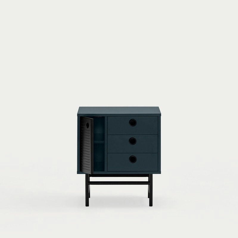 La mesita de noche Punto 1P3C es una mesita de noche pequeña de color verde oscuro con tres cajones y una puerta abierta sobre un marco negro, que ofrece un amplio espacio de almacenamiento interno. Su diseño contemporáneo agrega elegancia a cualquier habitación sobre un fondo liso.