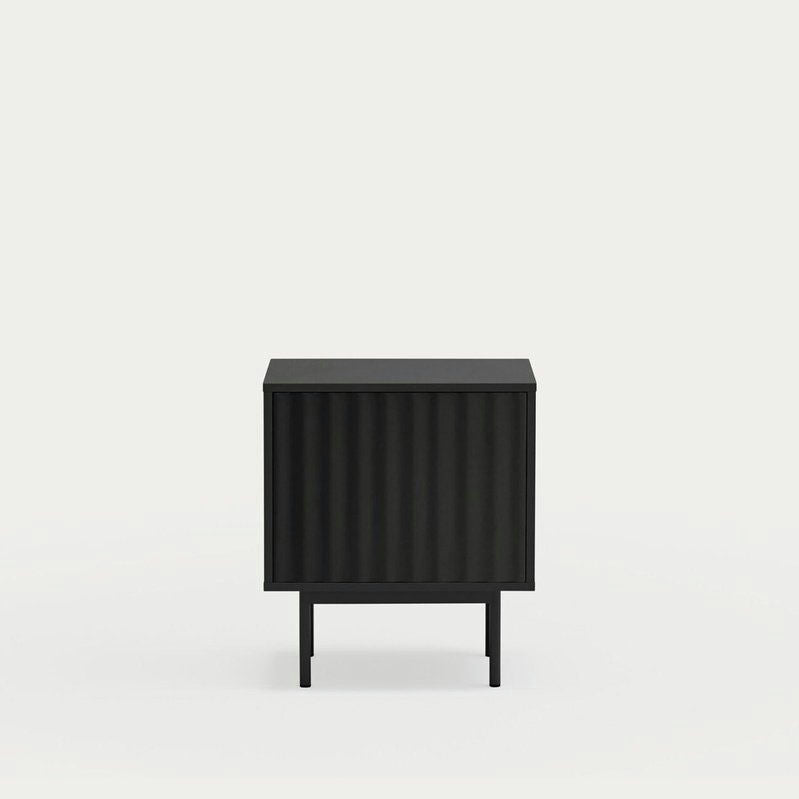 El gabinete cuadrado negro minimalista de Cambres Design tiene una textura acanalada vertical y se apoya sobre patas delgadas sobre un fondo blanco, ofreciendo un almacenamiento elegante como la Mesita de noche Sierra 2C.